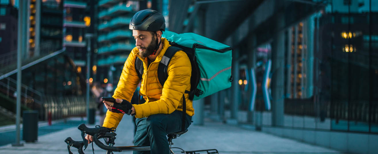 Courier cyclist in the city, checking his smartphone.